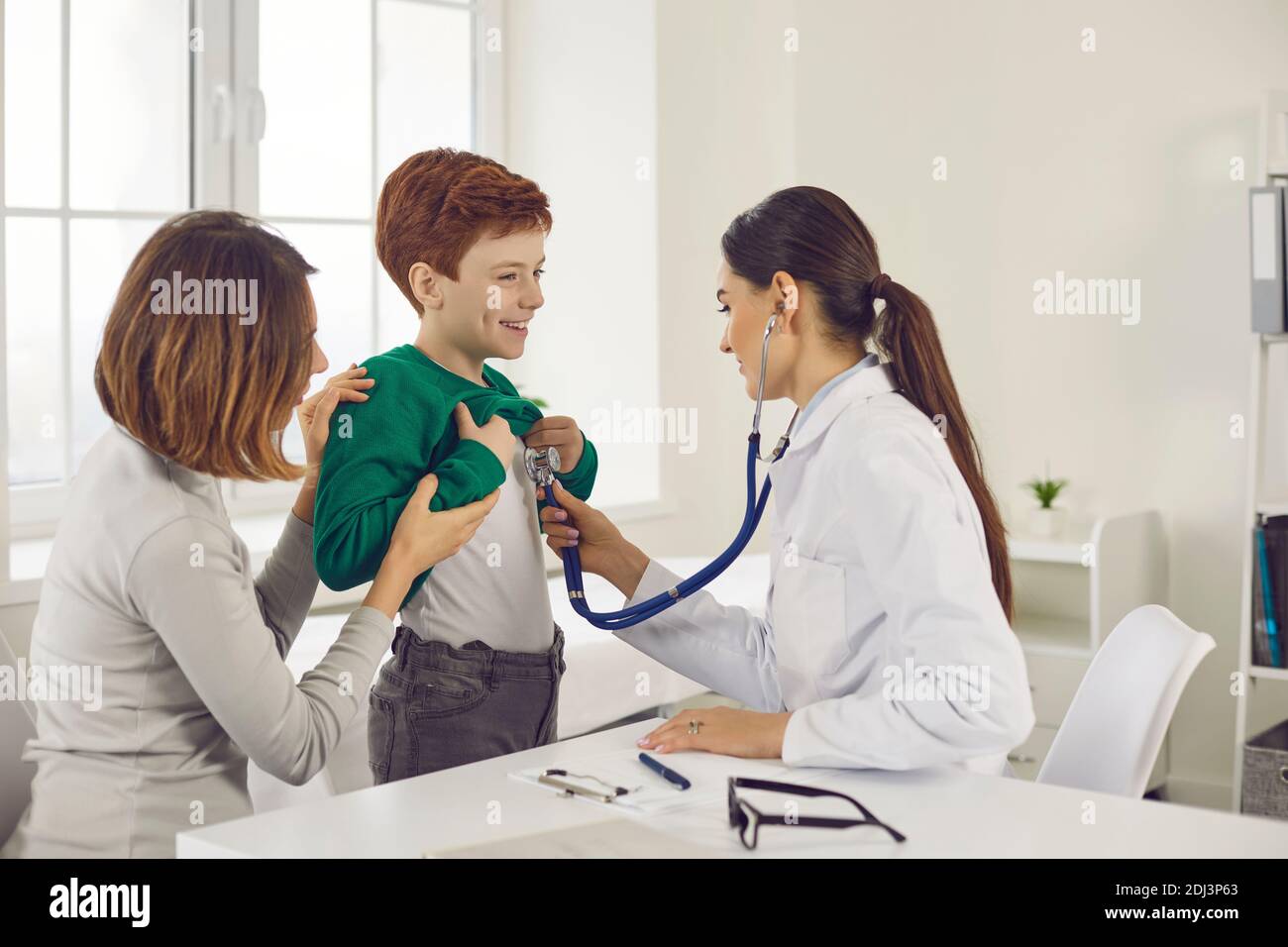 Der Arzt hört mit einem Stethoskop einem Jungen zu, der mit seiner Mutter zu einer medizinischen Untersuchung kam. Stockfoto