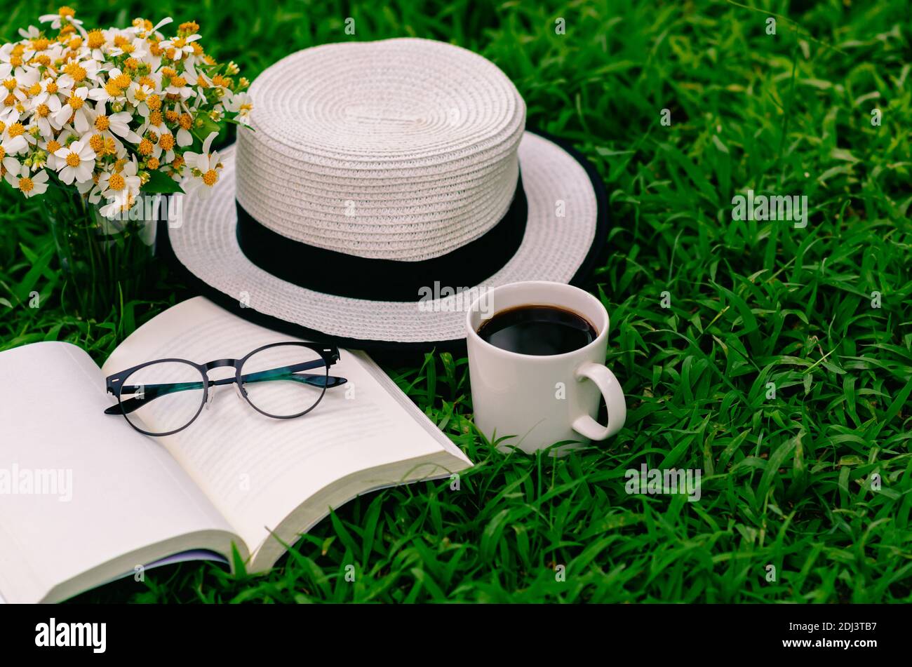 Freizeit am Morgen im Garten mit Kaffee, Buch, Hut und Blumen auf dem Rasen  Stockfotografie - Alamy