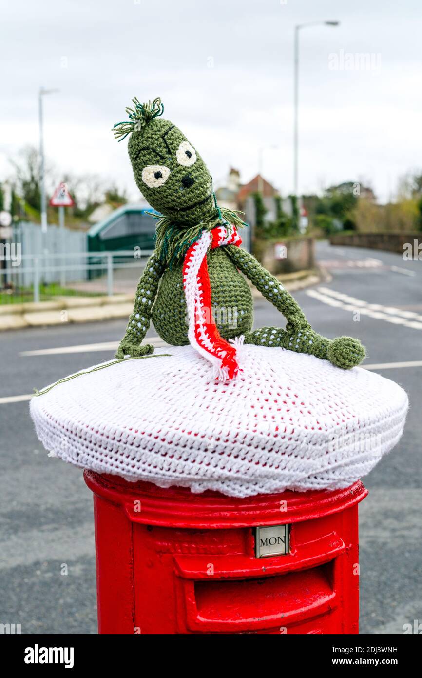 Britische traditionelle rote Briefkästen mit Strickmützen als Weihnachtsdekoration. Kermit der Frosch sitzt in einem Schal Stockfoto