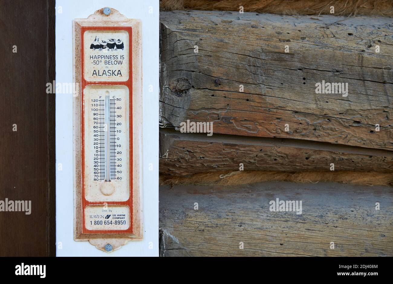 Historisches Thermometer mit der Aufschrift "Glück ist unter 50 Grad - Alaska" auf dem weißen Fensterrahmen eines Holzhauses montiert. Stockfoto