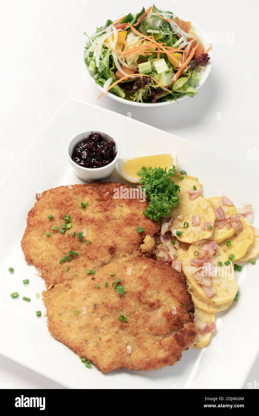 deutsche panierte Schweinefleischschnitzel mit Speck Bratkartoffeln Preiselbeersauce und Salat auf weißem Studiohintergrund Stockfoto