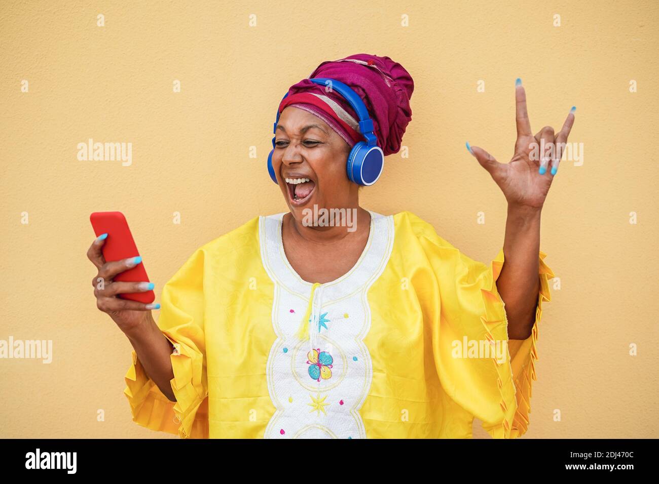 Schwarze ältere Frau auf traditionellen afrikanischen Kleid tanzen zu Rock Musik mit Mobiltelefon - Fokus auf Gesicht Stockfoto