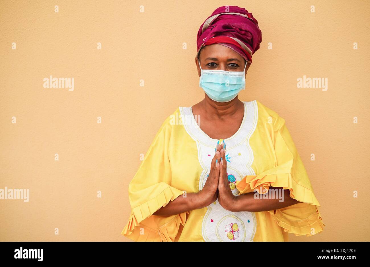 Ältere schwarze Frau hält die Hände in Gebetsstellung und trägt traditionell afrikanisches Kleid - Soziales Fernkonzept Stockfoto