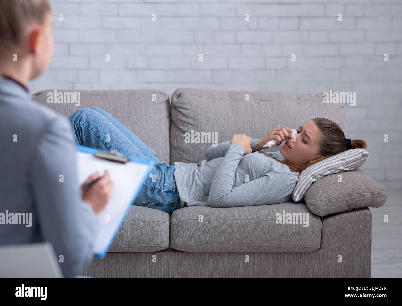 Deprimierte junge Frau, die Psychologin konsultiert, auf der Couch liegend und weinend Stockfoto