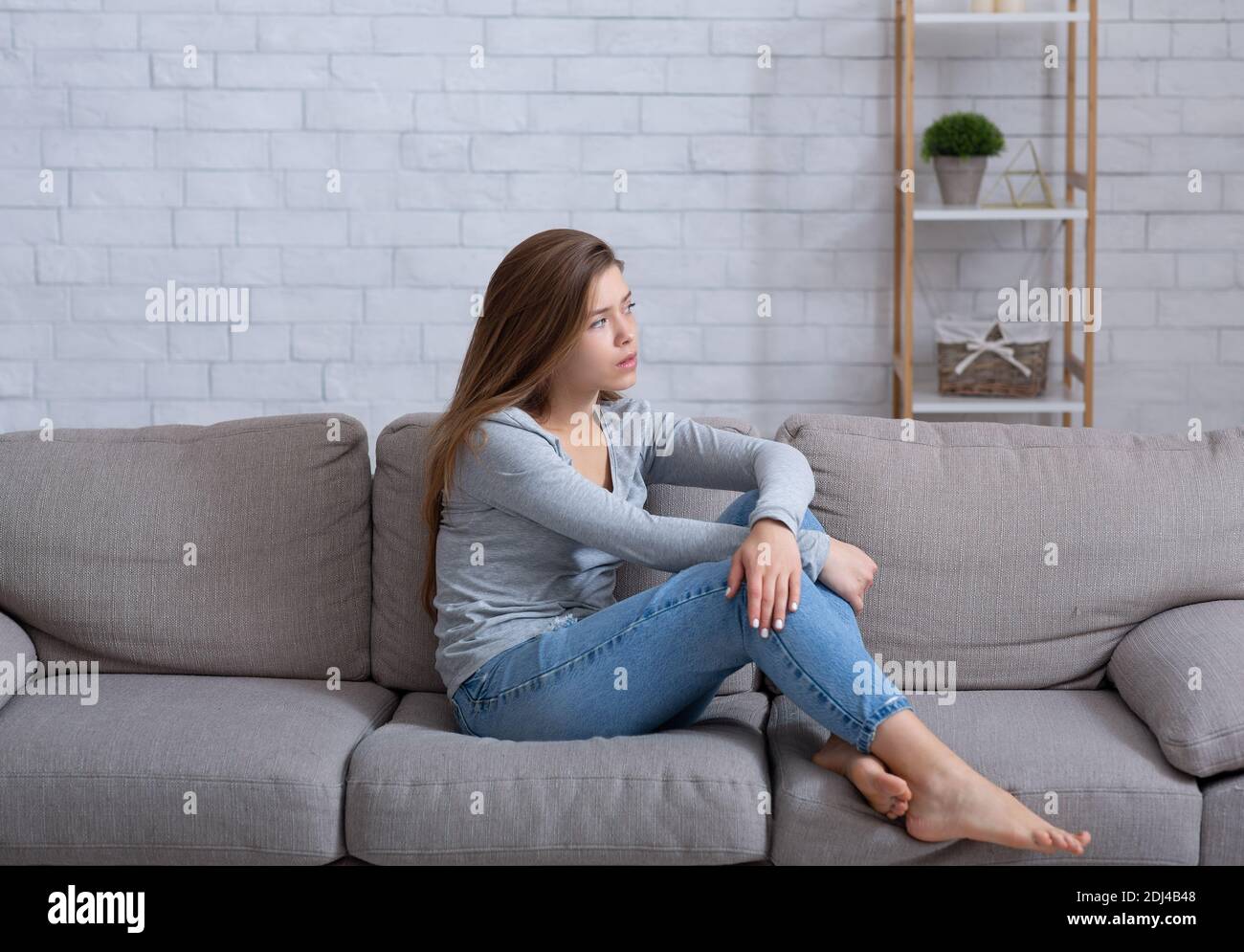 Einsame junge Dame, die zu Hause auf dem Sofa sitzt, sich deprimiert und frustriert fühlt, an emotionaler Erschöpfung leidet Stockfoto