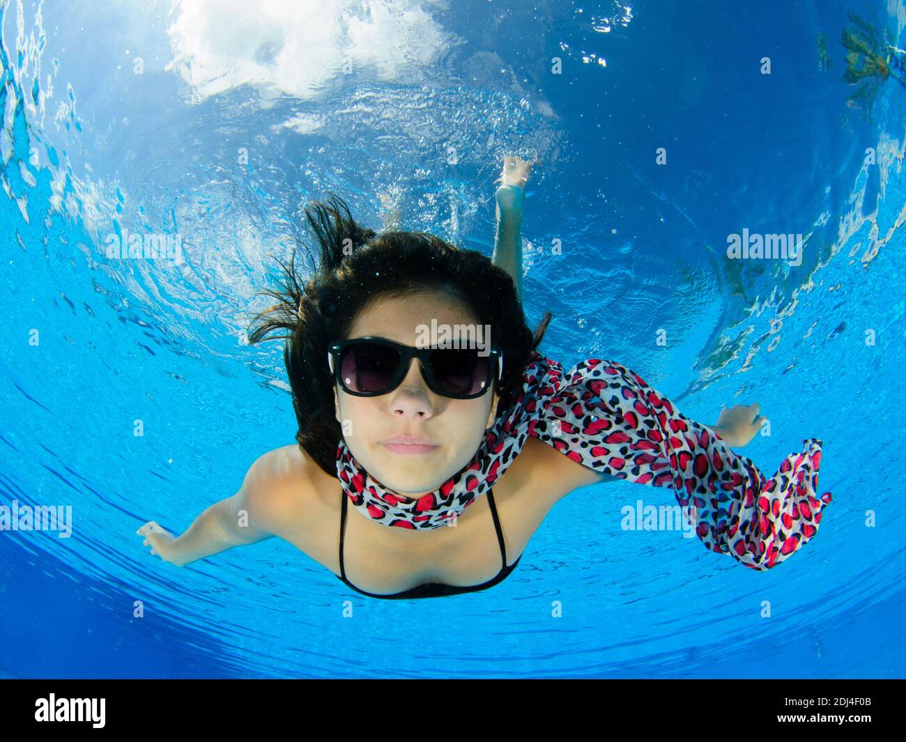 Eine 12-jährige weibliche Teenager Freitauchen unter Wasser in einem Schwimmbad mit einem bunten Schal und Sonnenbrille. Modellversion verfügbar Stockfoto