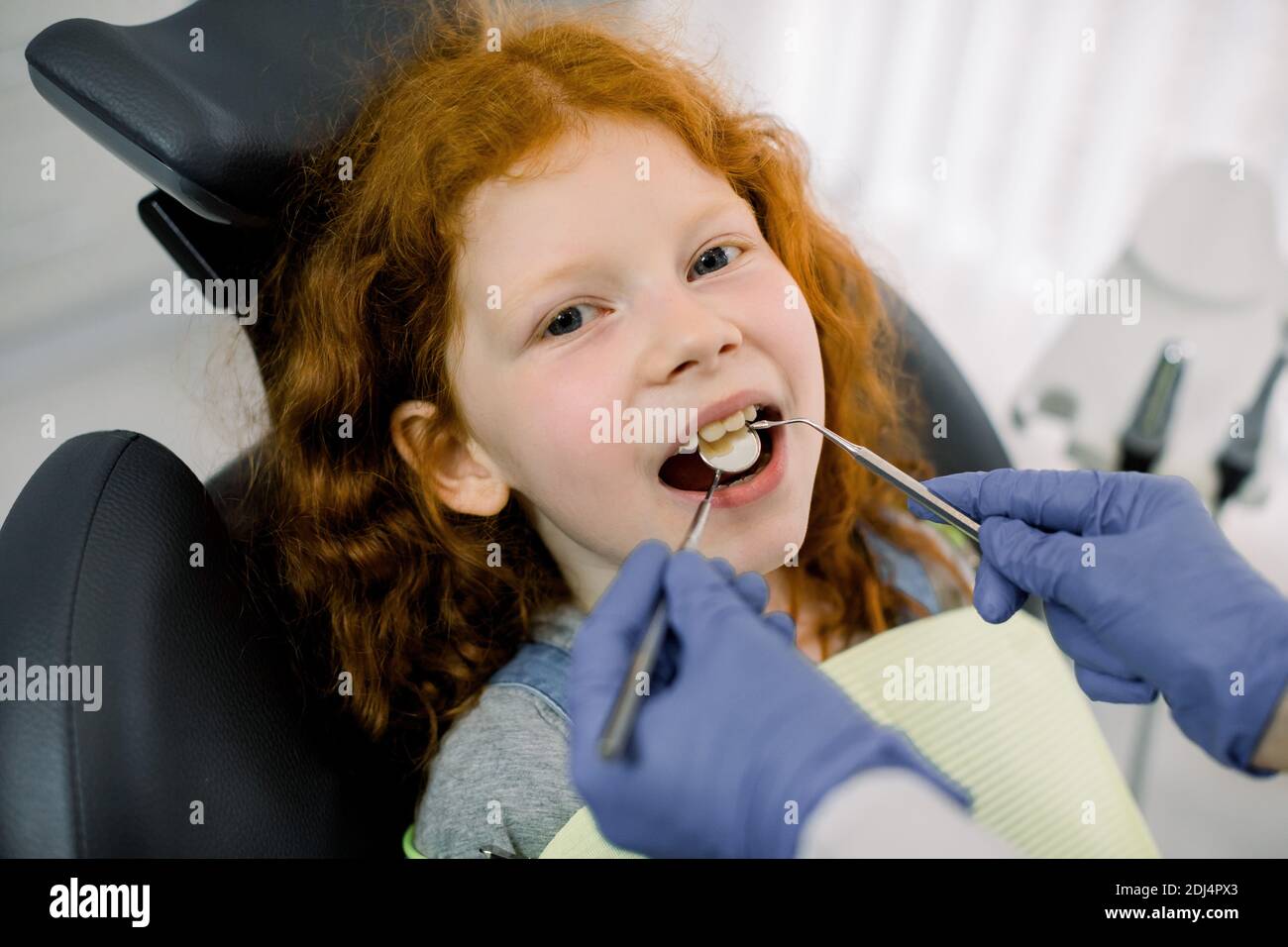 Ein Kind an der Zahnarztrezeption. Nahaufnahme Porträt von hübschen kleinen Mädchen mit roten lockigen Haaren, sitzen mit offenem Mund in Zahnarztstuhl, während Stockfoto