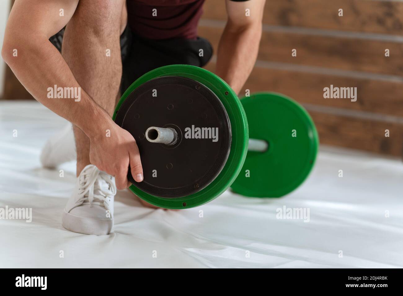 Hebe eine Langhantel jungen Mann Bogen auf dem Knie Hinzufügen oder Ändern von schwarzen und grünen Platten, Ausrüstung für Krafttraining Konzept. Sportausrüstung für Stockfoto