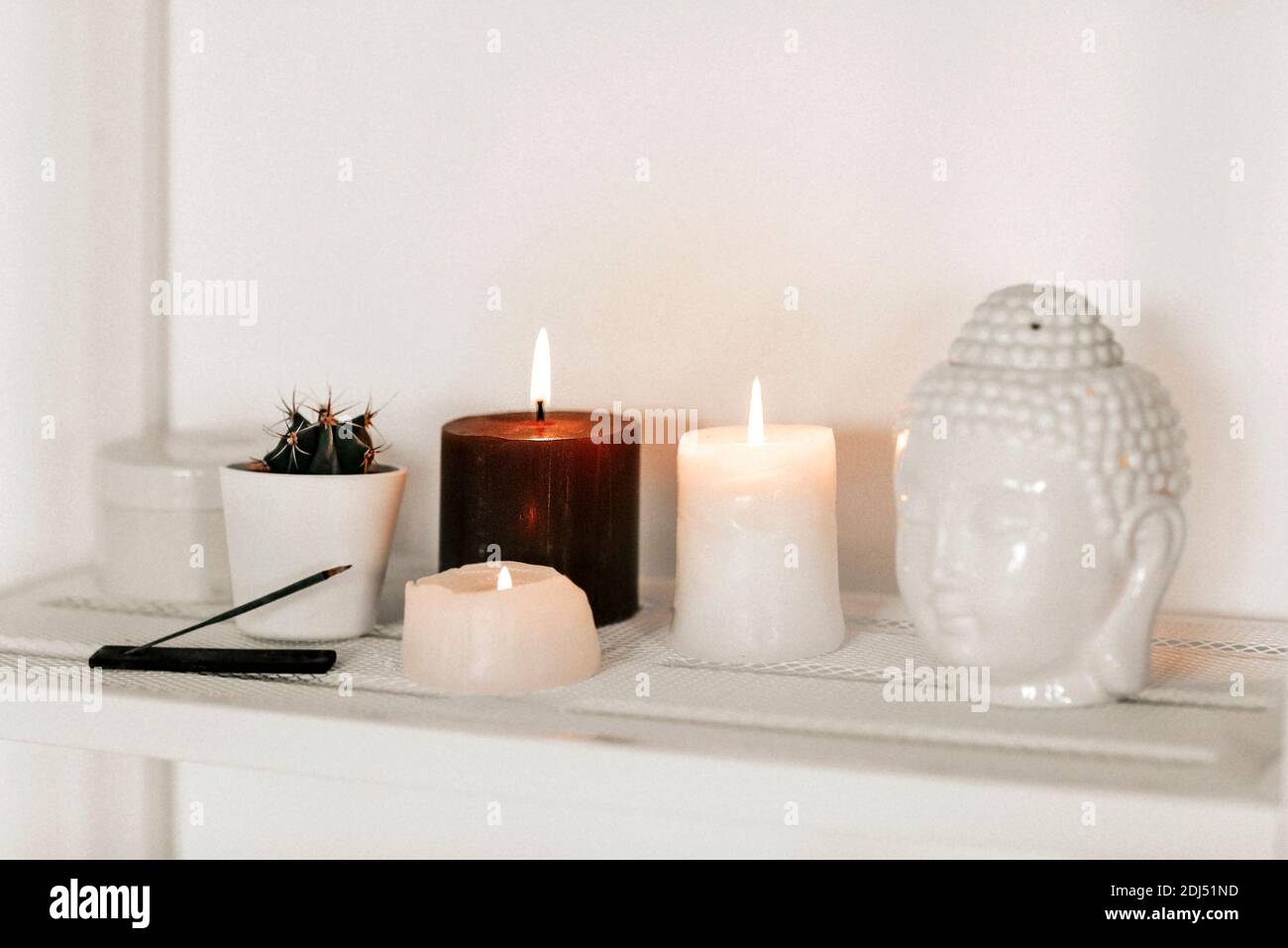 Brennende Kerzen und aromatischer Weihrauch auf Regal in der Nähe von  Topften platziert Kaktus und Keramik Buddha Kopf zu Hause Stockfotografie -  Alamy