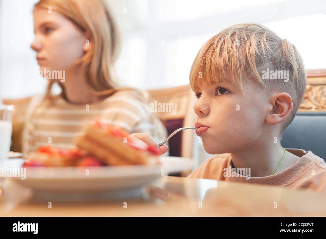 Portrait von niedlichen blonden Jungen Waffeln beim Familienfrühstück essen und wegschauen mit Löffel im Mund, kopieren Raum Stockfoto