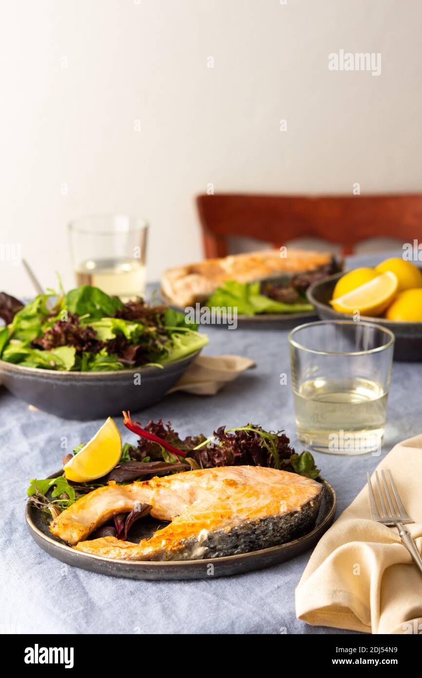 Gebratenes Lachssteak mit Salat auf einem Teller, Weißwein im Glas, leckeres herzhaftes Abendessen oder Mittagessen Stockfoto