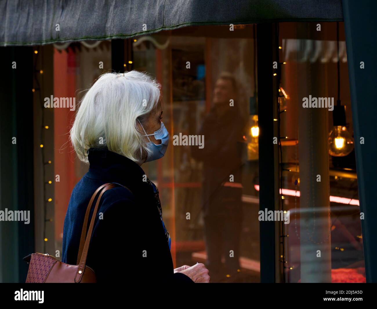 Ältere Frau, die eine Gesichtsmaske trägt, die darauf wartet, in ein Geschäft zu gehen, Bideford, Devon, Großbritannien, Weihnachten, 2020 Stockfoto