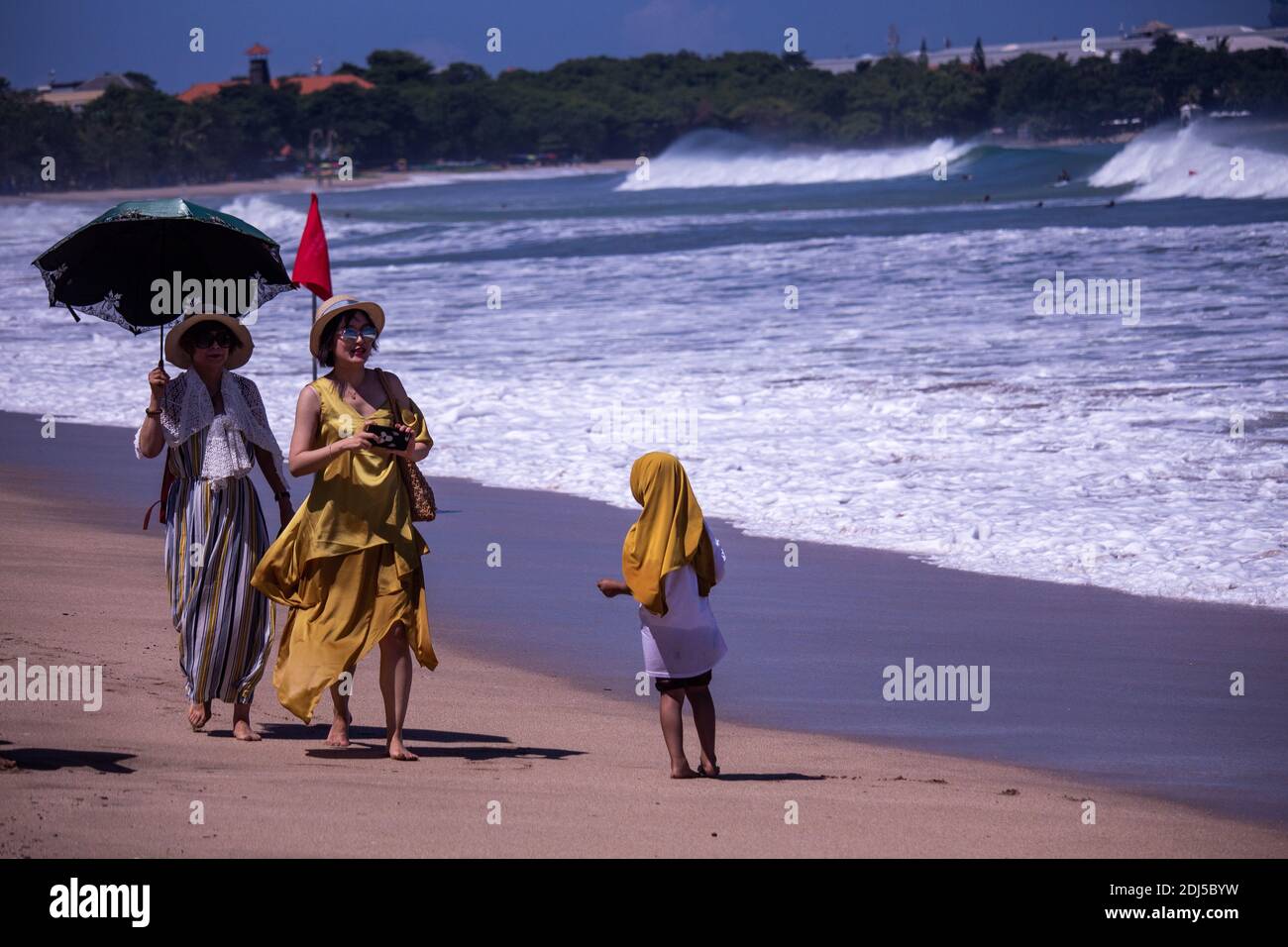 Kleines Mädchen, das von reichen chinesischen Touristen um Geld bettelte Ein Strand in Bali Stockfoto