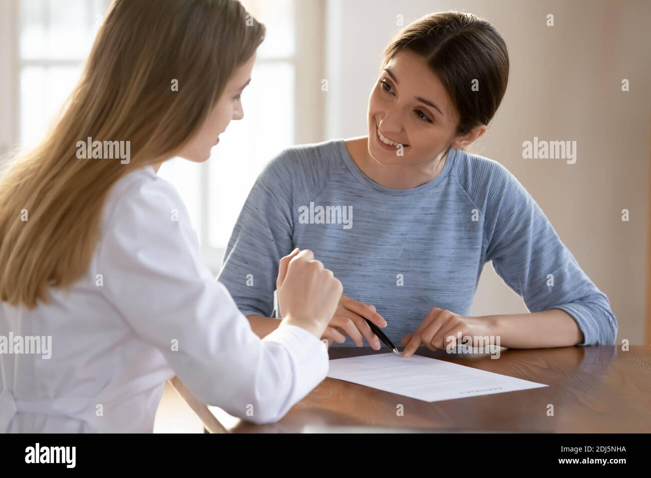 Lächelnde weibliche Patientin unterzeichnet Vertrag mit Arzt Stockfoto