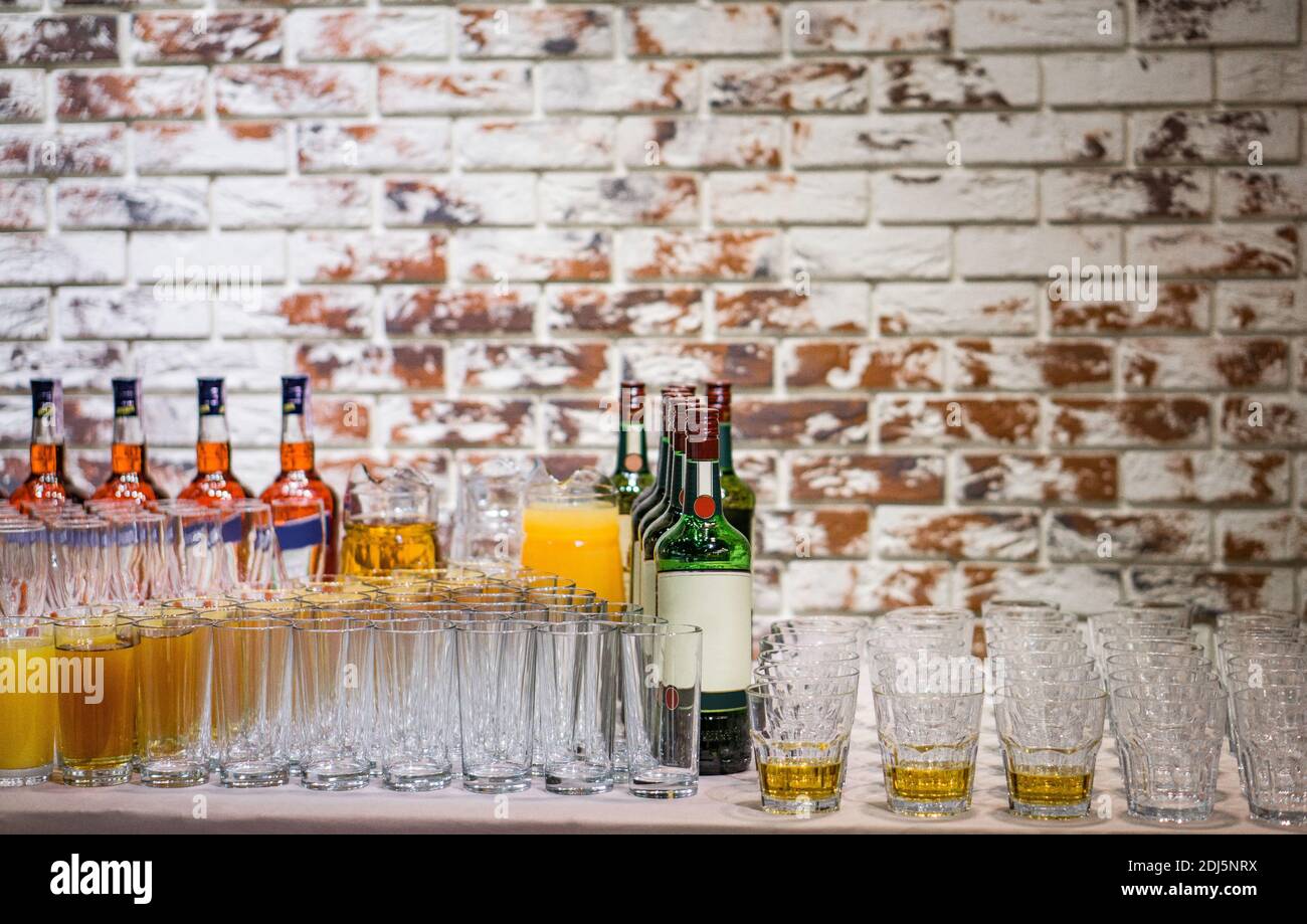 Leere und gefüllte Gläser neben Flaschen mit alkoholischen Getränken auf einem Backstein Wand Hintergrund. Vorbereitungen für Bankette oder Partys. Stockfoto