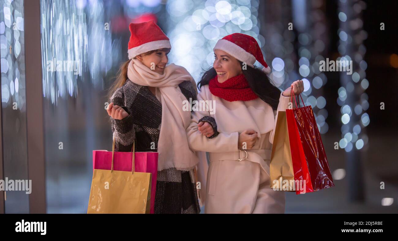 Zwei Frauen in Santa Hüte mit einer shopaholic Zeit mit vielen Geschenken bough für Weihnachten in bunten Papiertüten. Stockfoto