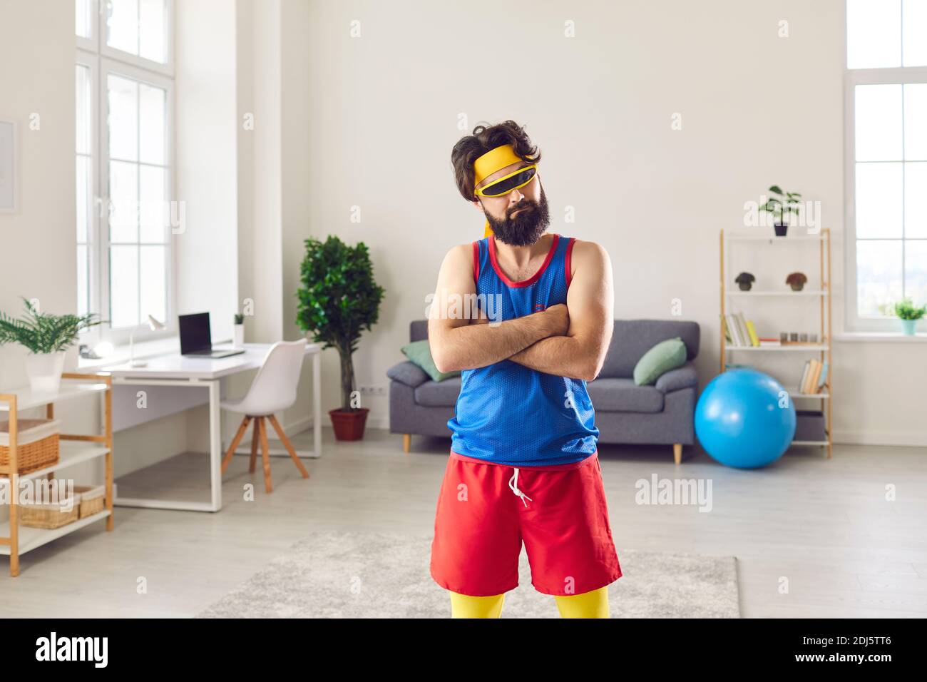 Lustiger wütender Mann in cooler Sonnenbrille und farbenfroher Retro-Sportbekleidung Stehende Arme im Wohnzimmer gefaltet Stockfoto