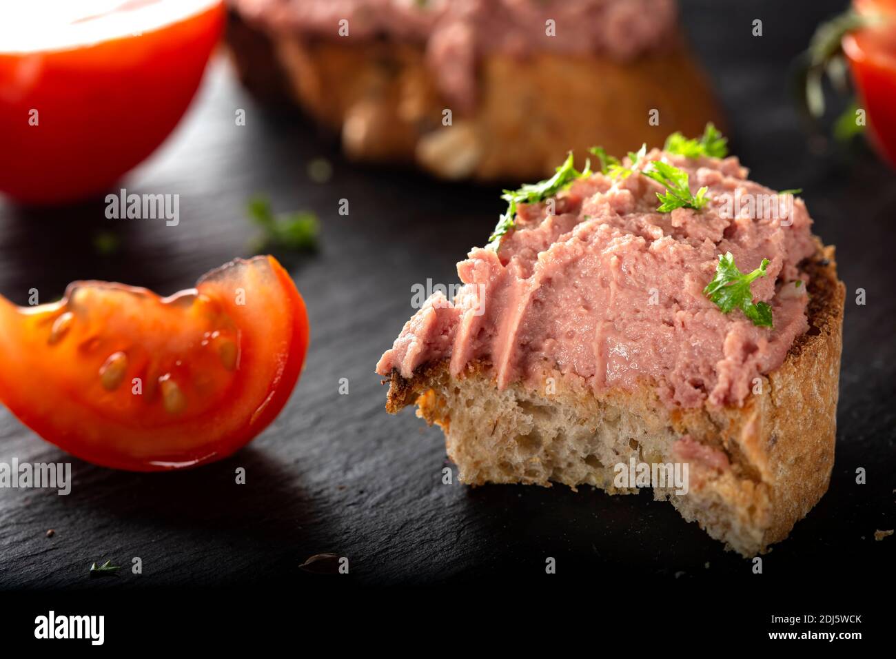 Gebissen Toast mit Schweinpastete, Tomaten und Kräutern auf dunklem Schiefer - Nahaufnahme Stockfoto