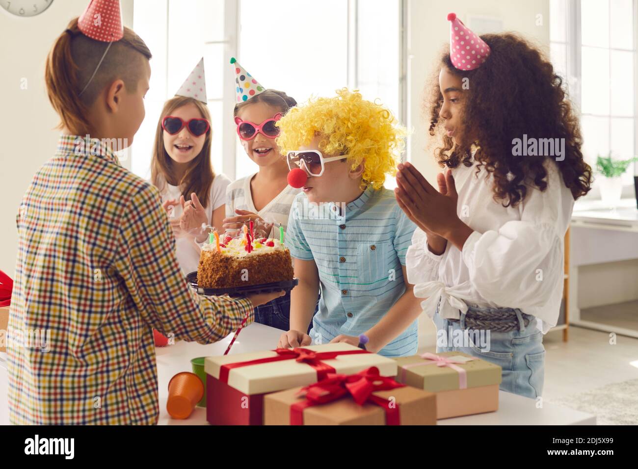 Gruppe von Kindern gratuliert ihrem Freund zu seinem Geburtstag und gibt ihm Geschenke und einen Kuchen. Stockfoto