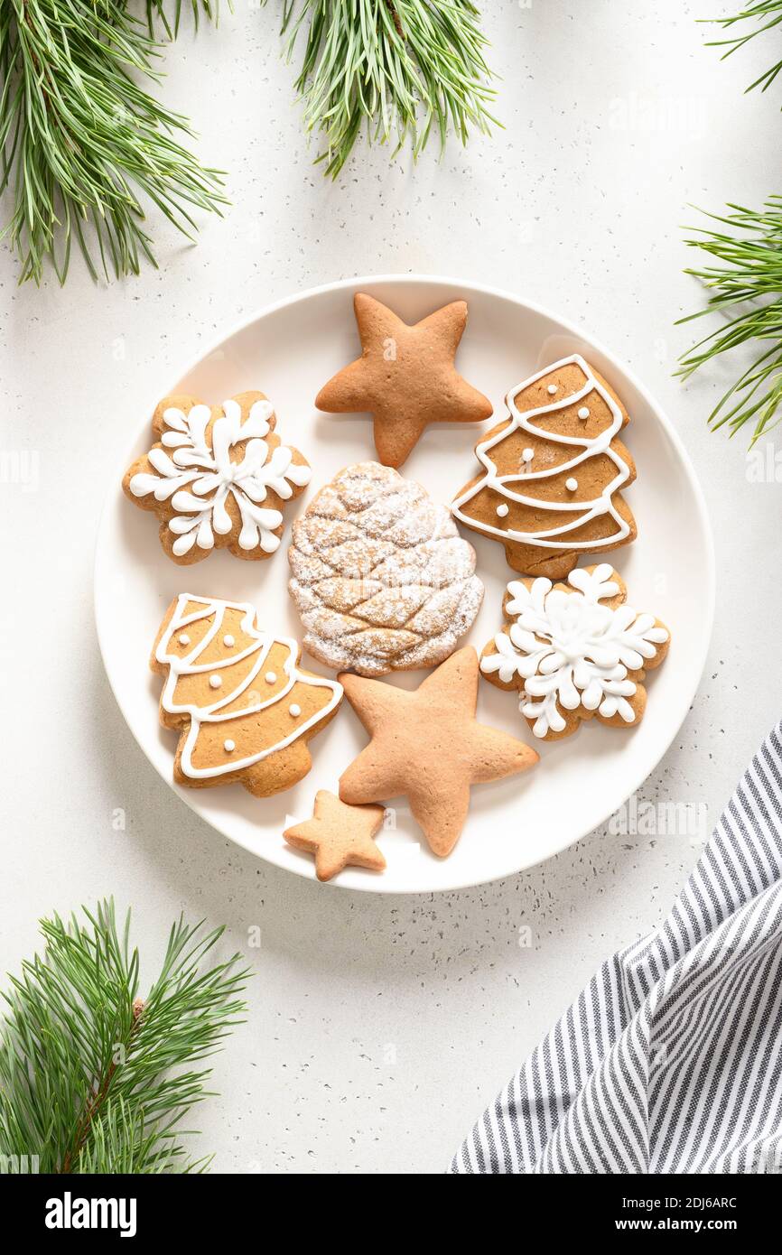Weihnachten handgemachte glasierte Kekse in Teller dekoriert Tannenzweige auf weißem Hintergrund. Blick von oben. Vertikales Format. Stockfoto