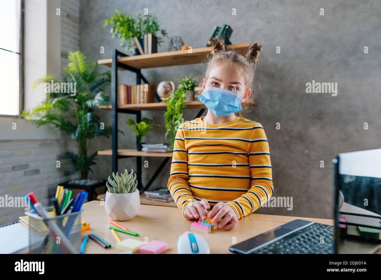 8 Jahre altes Mädchen in der medizinischen Einweg-Gesichtsmaske studieren online von zu Hause aus mit Laptop im Zimmer. Fernunterricht während Pandemiesperre c Stockfoto