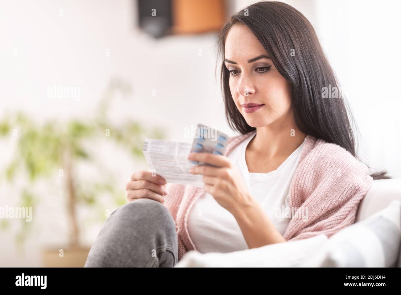 Frau liest Anweisungen vor der Einnahme von Medikamenten auf einem Sofa zu Hause. Stockfoto