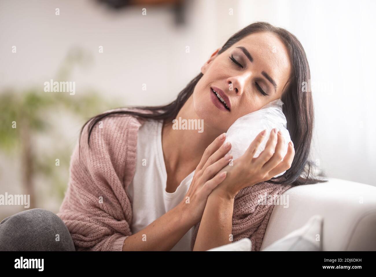 Gesichtsausdruck einer jungen Frau, die Eisbeutel auf der Wange hält. Stockfoto