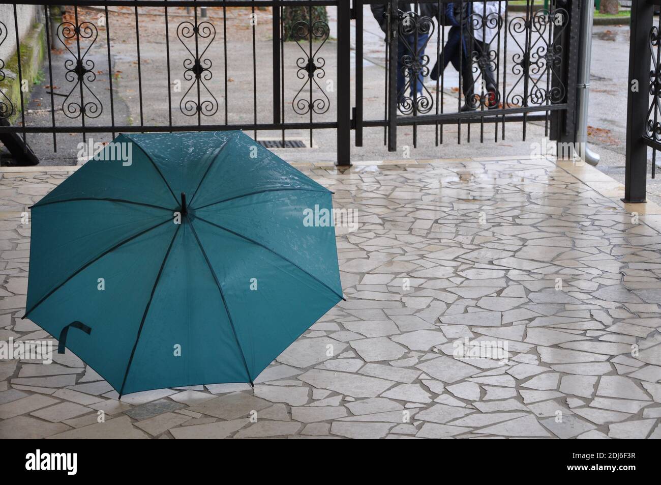 Blauer Regenschirm auf nassem Boden. Blauer Regenschirm auf dem nassen beigen Pflaster während eines regnerischen Tages. Stockfoto
