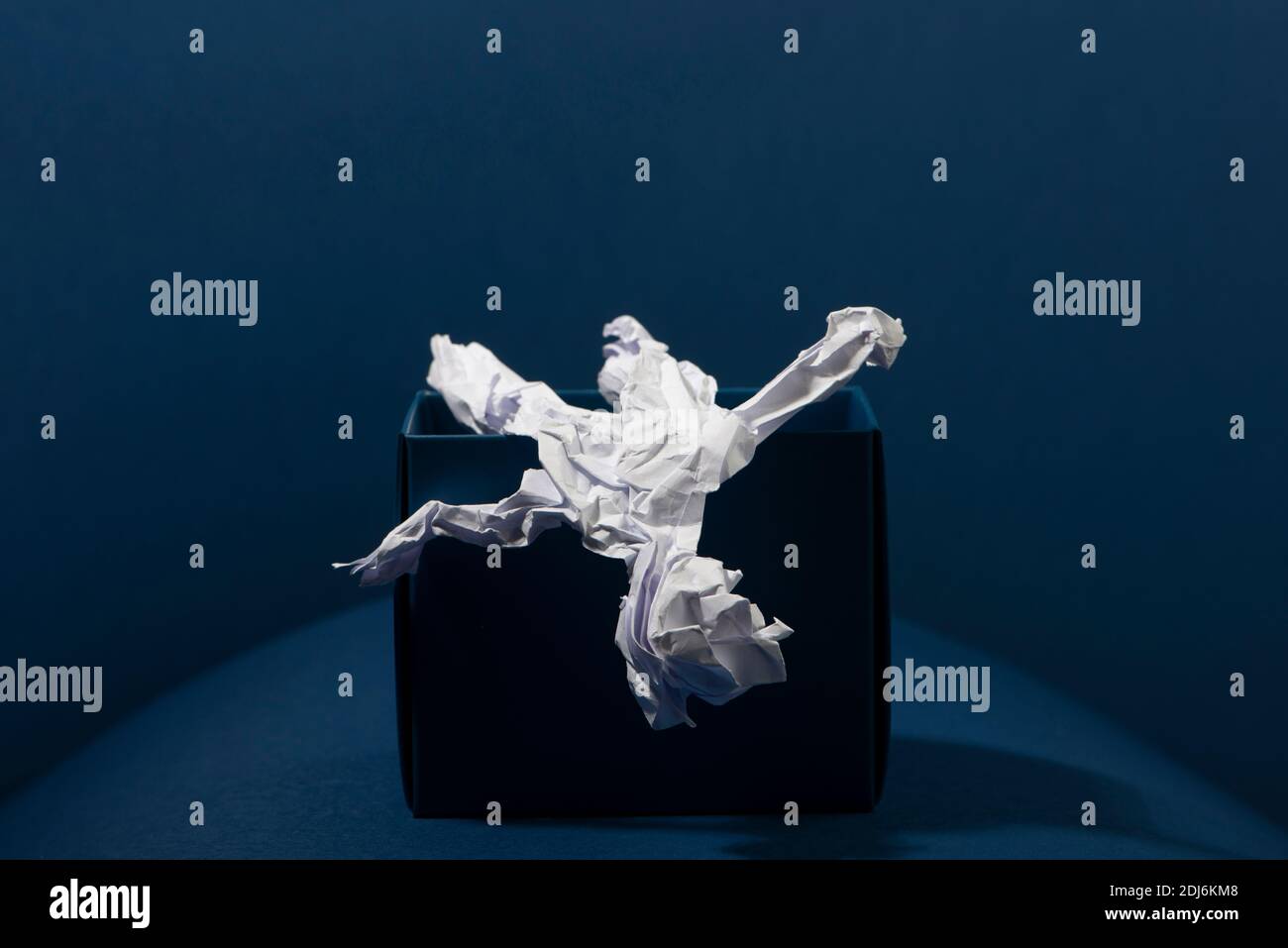 Papier menschliche Figur fällt aus einer schwarzen Box auf blauem Hintergrund. Blauer Montag. Stockfoto