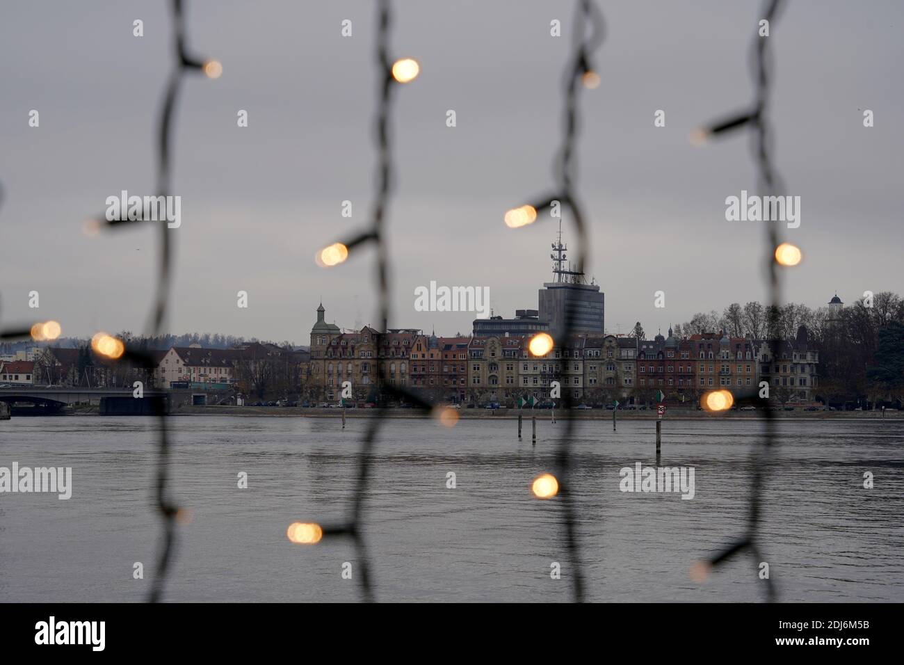 City Skyline am Ufer des Bodensees in Deutschland mit Silhouette von Weihnachtslichtern im Vordergrund. Saisonale Dekoration im Freien. Stockfoto