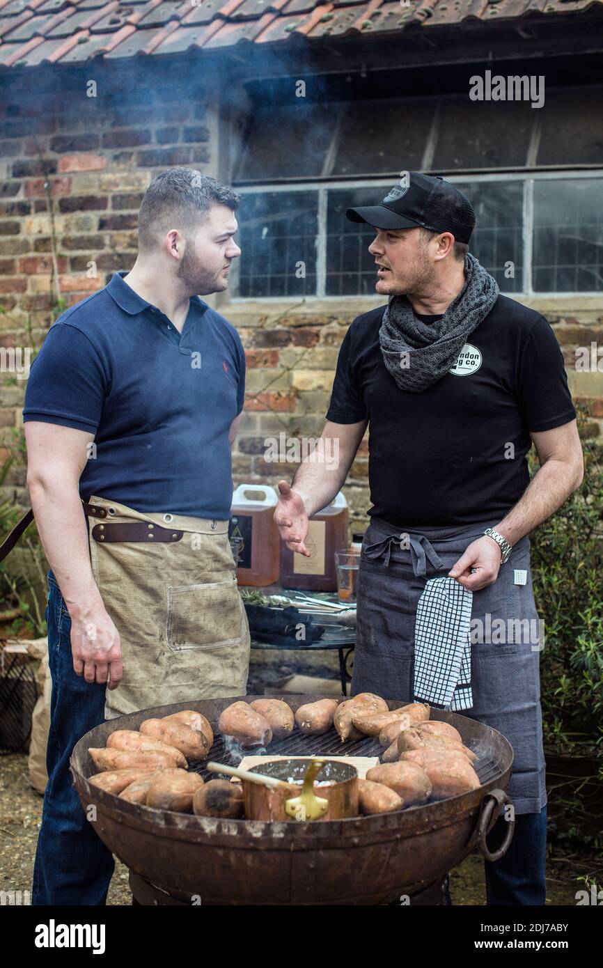 Zwei Männer, die sich unterhalten, während sie in einem Hinterhof vegan grillen.Gegrillte Süßkartoffeln. Stockfoto