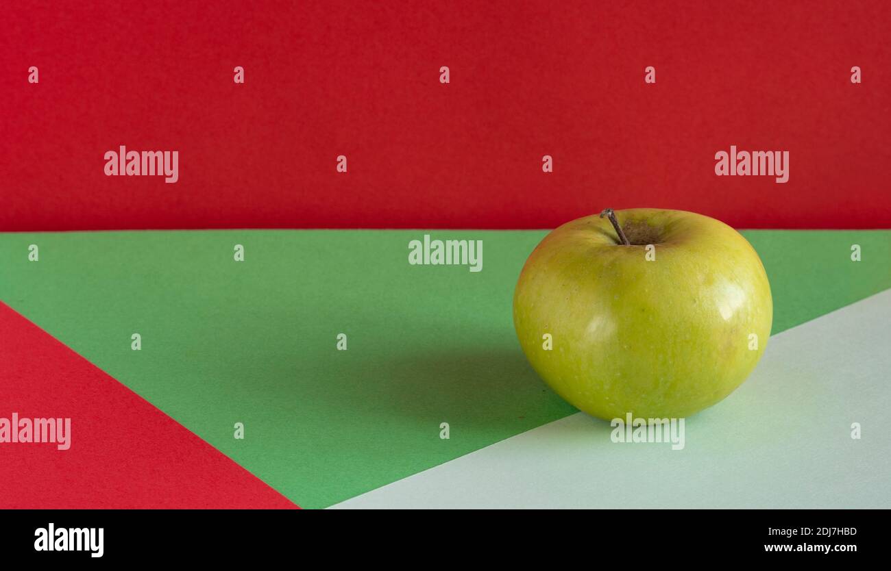 Grüner Apfel. Grüner Apfel auf einem roten, grün weißen Hintergrund. Stockfoto