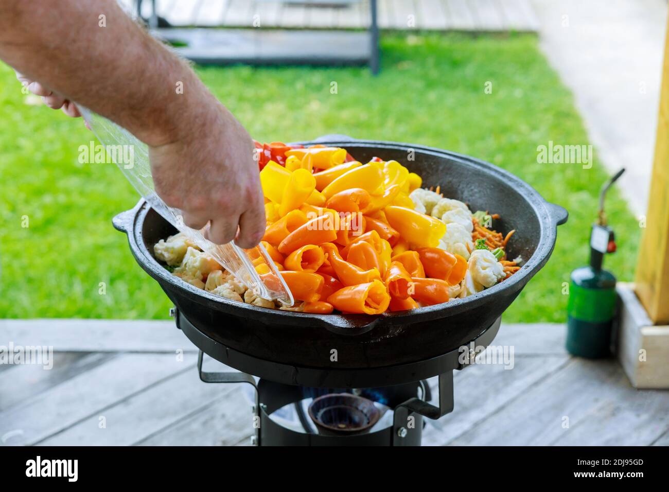 Mann Gießen Paprika in großen Kessel mit einem frischen gesunden Gemüse für Party im Freien. Stockfoto