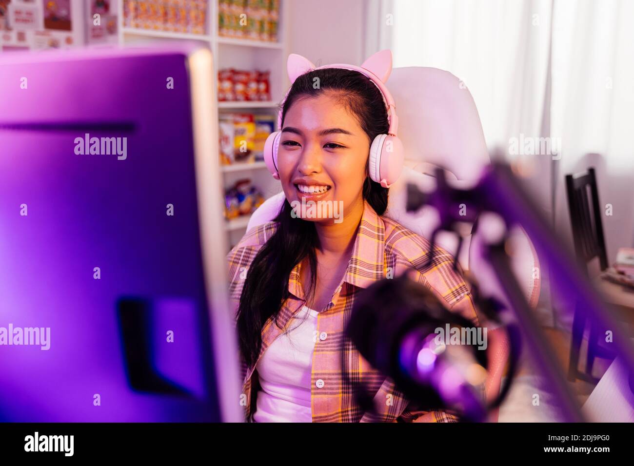 Aufgeregt und lächelnd Gamer Mädchen in niedlichen Headset mit einem Mikrofon spielen ein Online-Videospiel und Live-Streaming. Junge asiatische Frau im Gespräch mit Spielern und Publikum am Computer in neon LED-Licht-Raum zu Hause Stockfoto