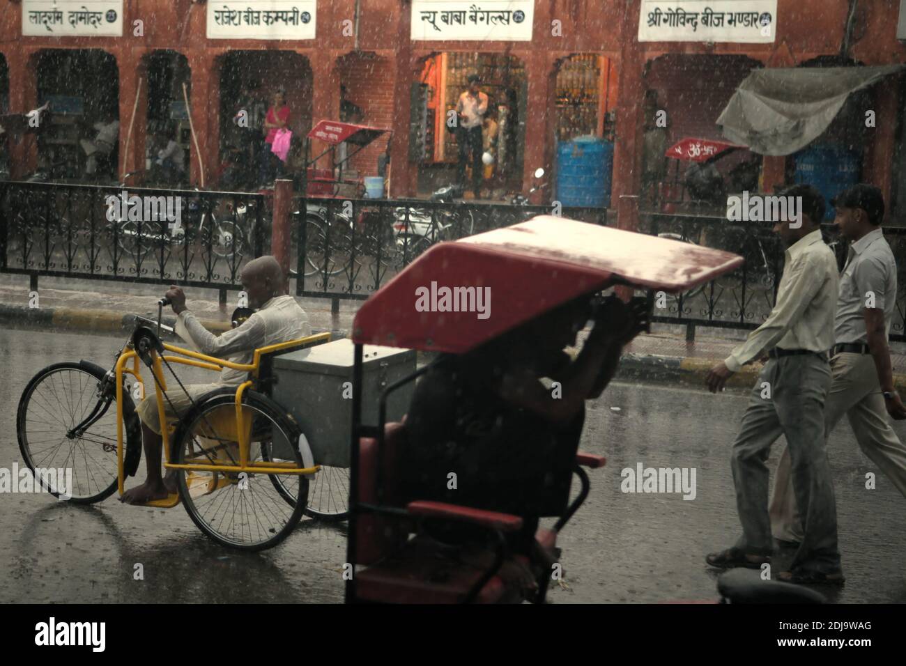 Männer zu Fuß, Radfahren auf der Straße während eines regnerischen Tages in Jaipur, Rajasthan, Indien. Stockfoto