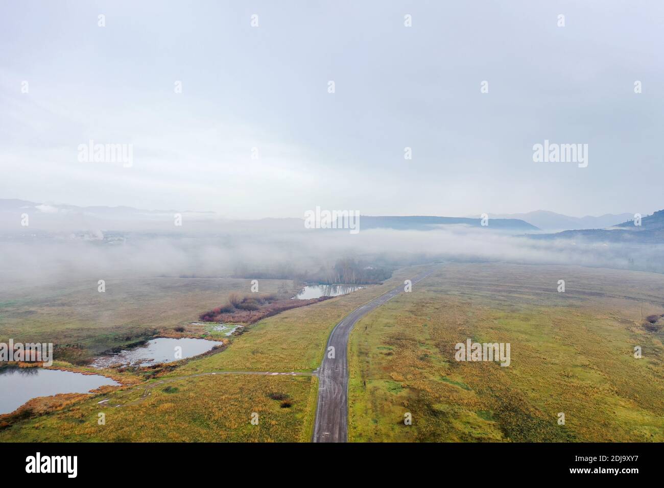 Straße in der Mitte eines grünen Feldes unter einem Nebliger und wolkiger Himmel Stockfoto