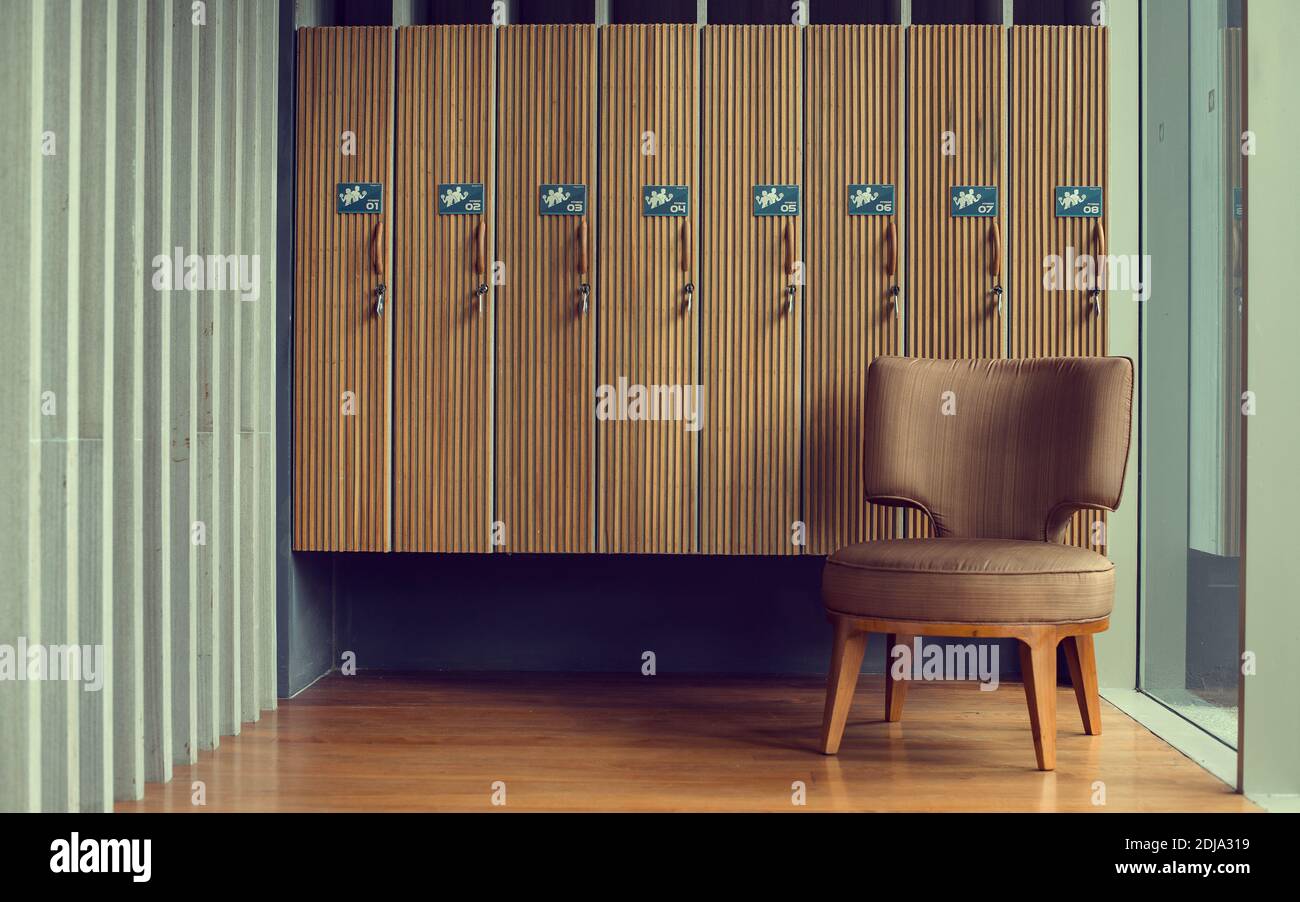Umkleideraum mit braunem Stuhl und hölzernen Schließfächern im Fitnessraum. Stockfoto