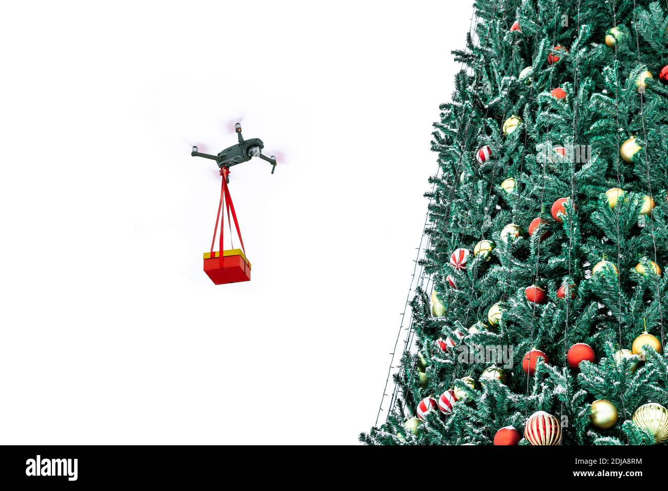 Eine Drohne fliegt mit einem Weihnachtsgeschenk auf dem Hintergrund eines Weihnachtsbaums. Stockfoto