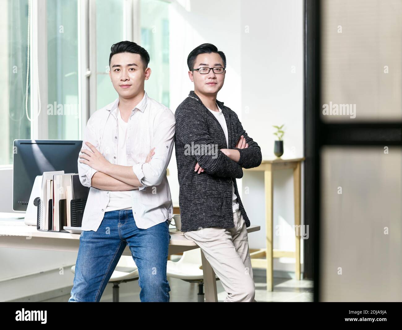 Portrait von zwei jungen asiatischen Geschäftsmännern, die sich zurück zu posieren Zurück im Büro mit Blick auf die Kamera Stockfoto