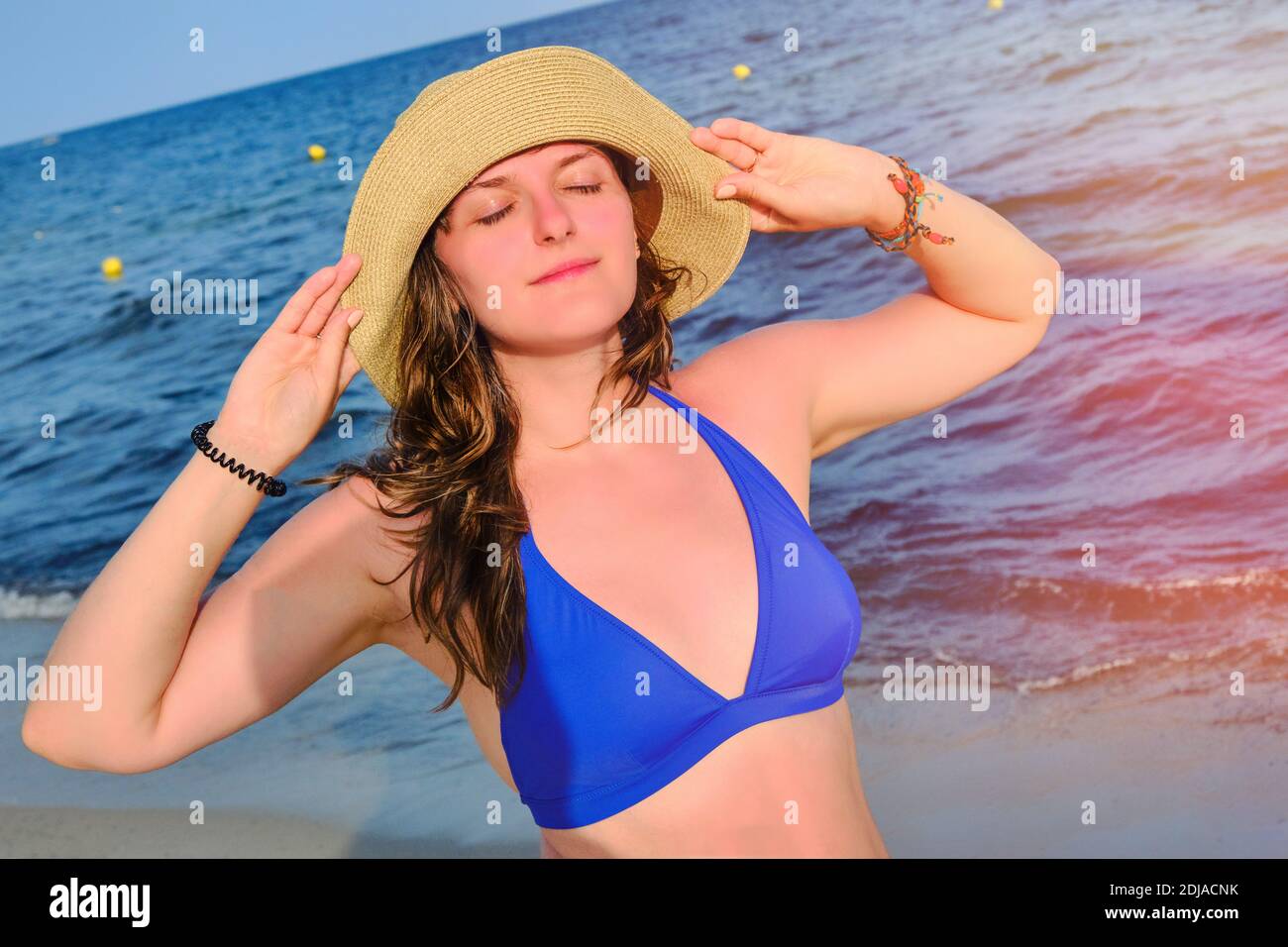 Eine junge Frau in einem Strohhut drehte ihr Gesicht Zur Sonne gegen das  Meer Stockfotografie - Alamy