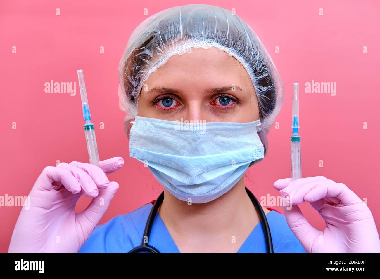 Ärztin in einer medizinischen Maske auf rotem Hintergrund mit Spritzen in den Händen. Medic mit Coronavirus-Impfstoff, Konzept der Medikamente gegen Influenza vi Stockfoto