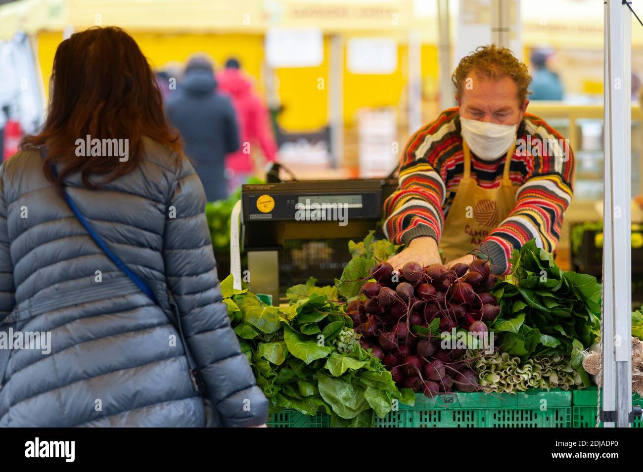 Gemüsehändler mit Schutzmaske greift eine Handvoll frischer Rote Bete. Stockfoto