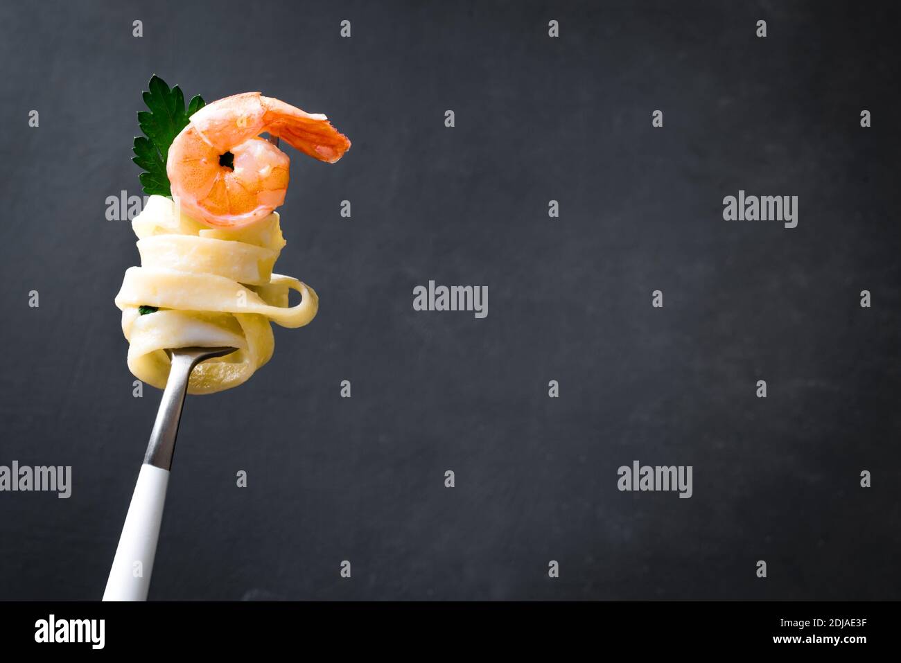 Gabel mit Nudeln und Garnelen auf dunklem Hintergrund, Kopierplatz. Fettuccine Pasta mit Sahne alfredo Sauce und Garnelen auf Gabel aus nächster Nähe. Stockfoto