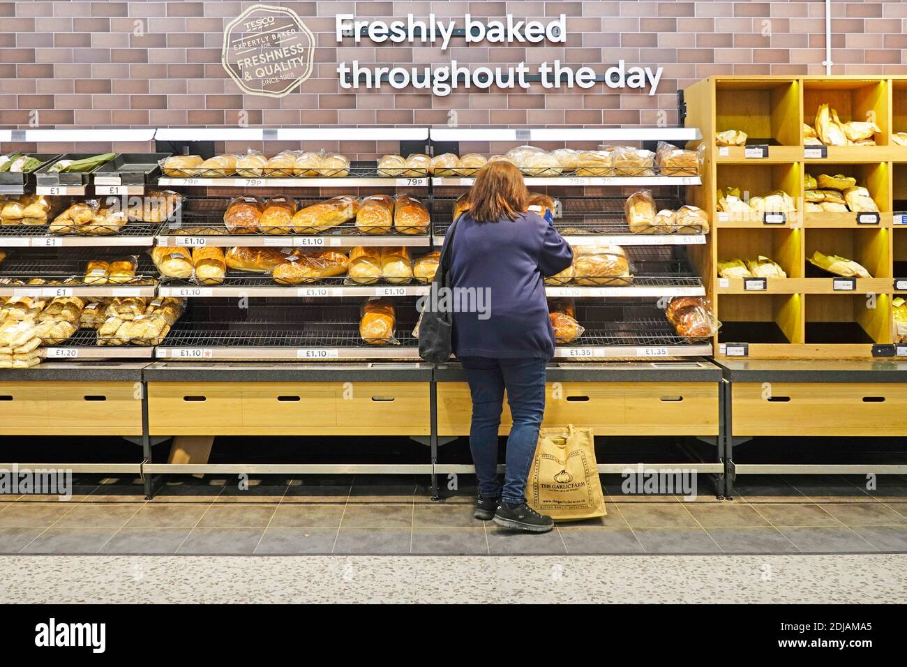 Rückansicht des Kunden beim Broteinkauf im Tesco Supermarkt Im Geschäft Bäckerei Auswahl Regale unten Zeichen für frisch gebacken Den ganzen Tag London England Großbritannien Stockfoto