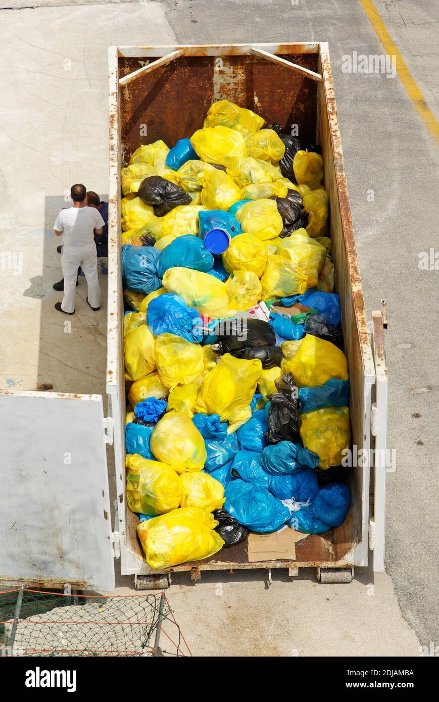 Luftaufnahme blau & gelb Kunststoff Müllsäcke von Besuch Kreuzfahrtschiff-Liner in rostigen Müll überspringen zwei Arbeiter stehen Im Schatten am Seehafen-Steg Stockfoto