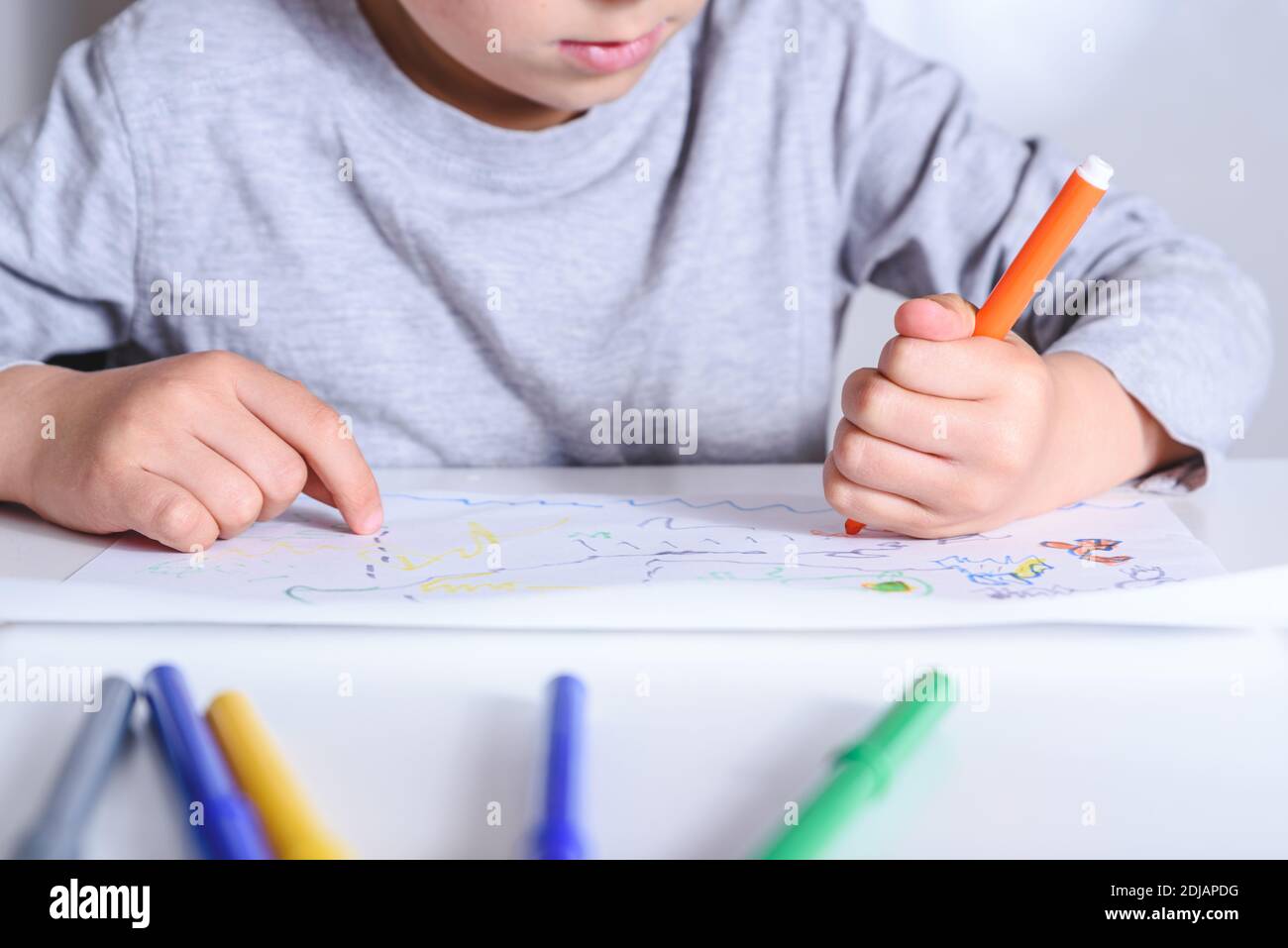 Detail der Hand eines linken Hand nicht erkennbar kaukasischen Kind Zeichnung mit Farbe Filz Stifte auf einem Papier auf der Oberseite eines weißen Tisch. Selektiver Fokus Stockfoto