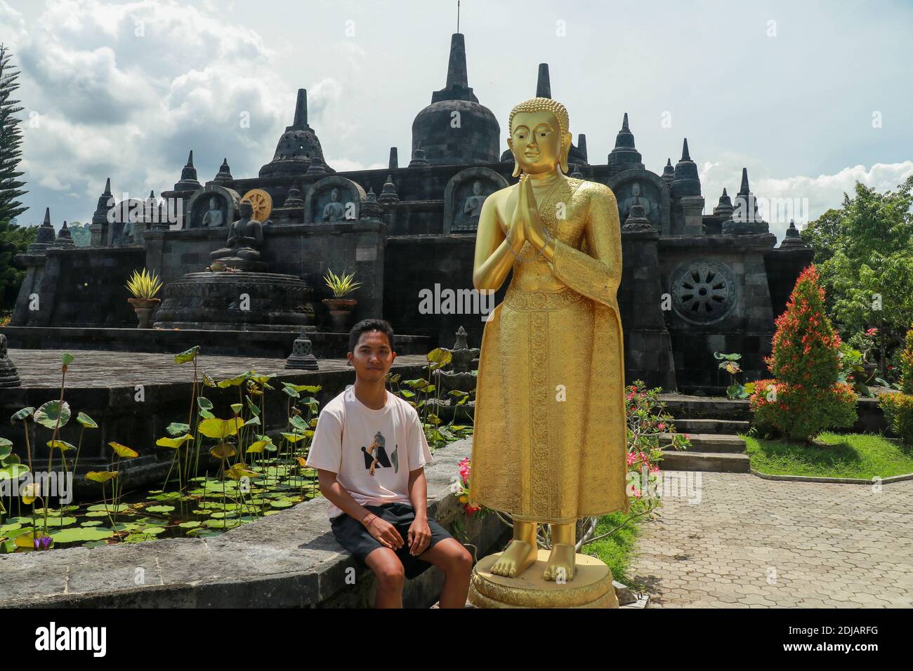 Asiatischer männlicher Tourist in einem buddhistischen Tempel. Ein junger Mann in einem Hemd mit goldener buddha-Statue. Auf dem Hintergrund der Sehenswürdigkeiten des Brahma vihara Arama Stockfoto