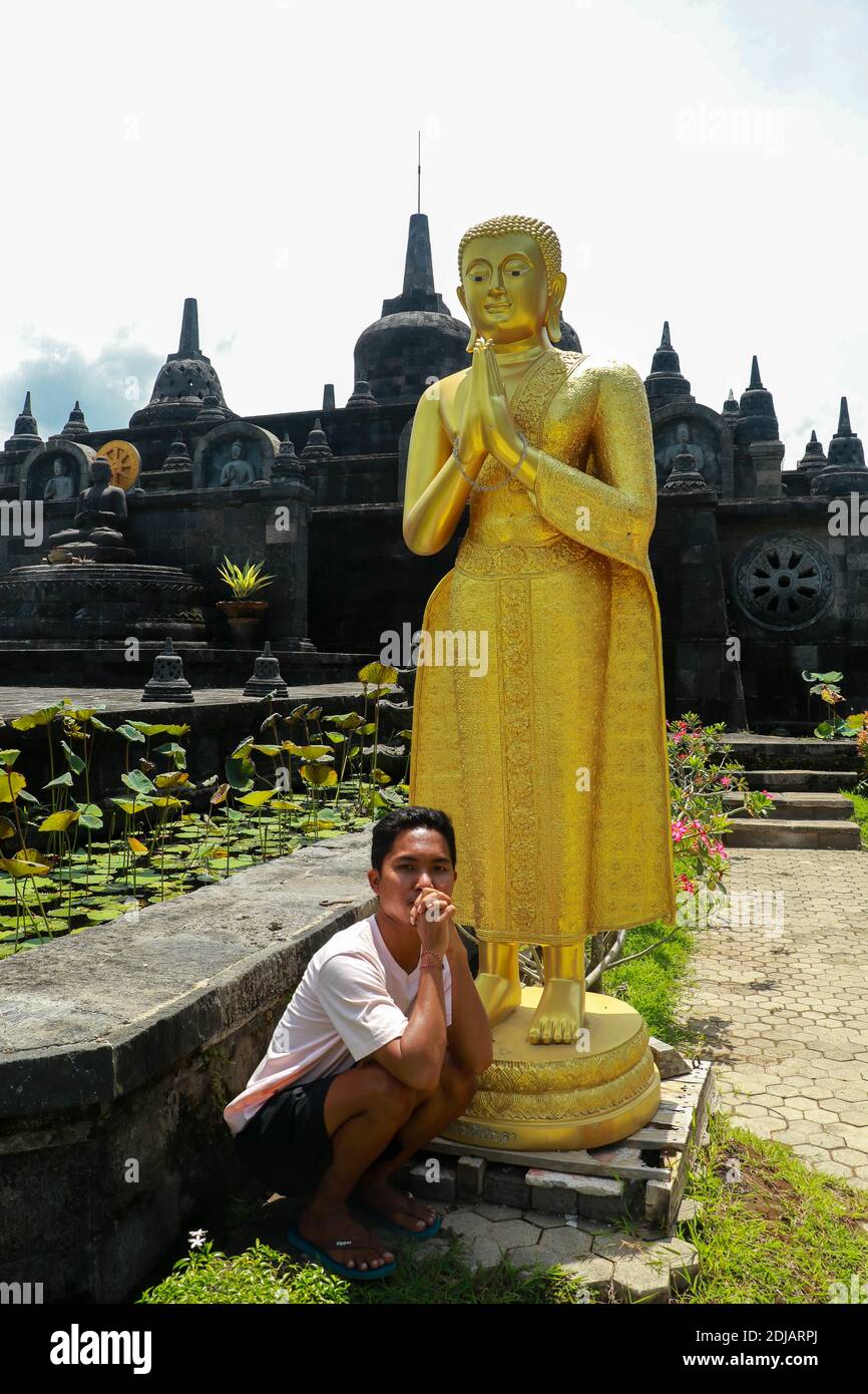 Asiatischer männlicher Tourist in einem buddhistischen Tempel. Ein junger Mann in einem Hemd mit goldener buddha-Statue. Auf dem Hintergrund der Sehenswürdigkeiten des Brahma vihara Arama Stockfoto