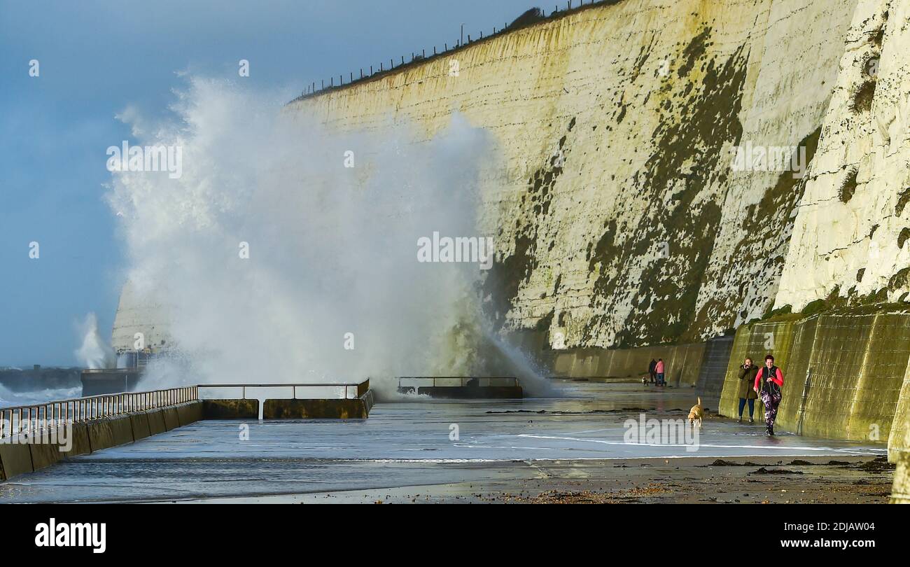 Brighton UK 14. Dezember 2020 - Wanderer und Läufer weichen den Wellen aus, die heute bei Flut bei Saltdean undercliff Walk in der Nähe von Brighton einstürzen. Die Wettervorhersage ist für stärkere Winde und Duschen, um über Teile von Großbritannien zu verbreiten, aber mit Temperaturen, die wärmer als in den letzten Tagen sind : Credit Simon Dack / Alamy Live News Stockfoto