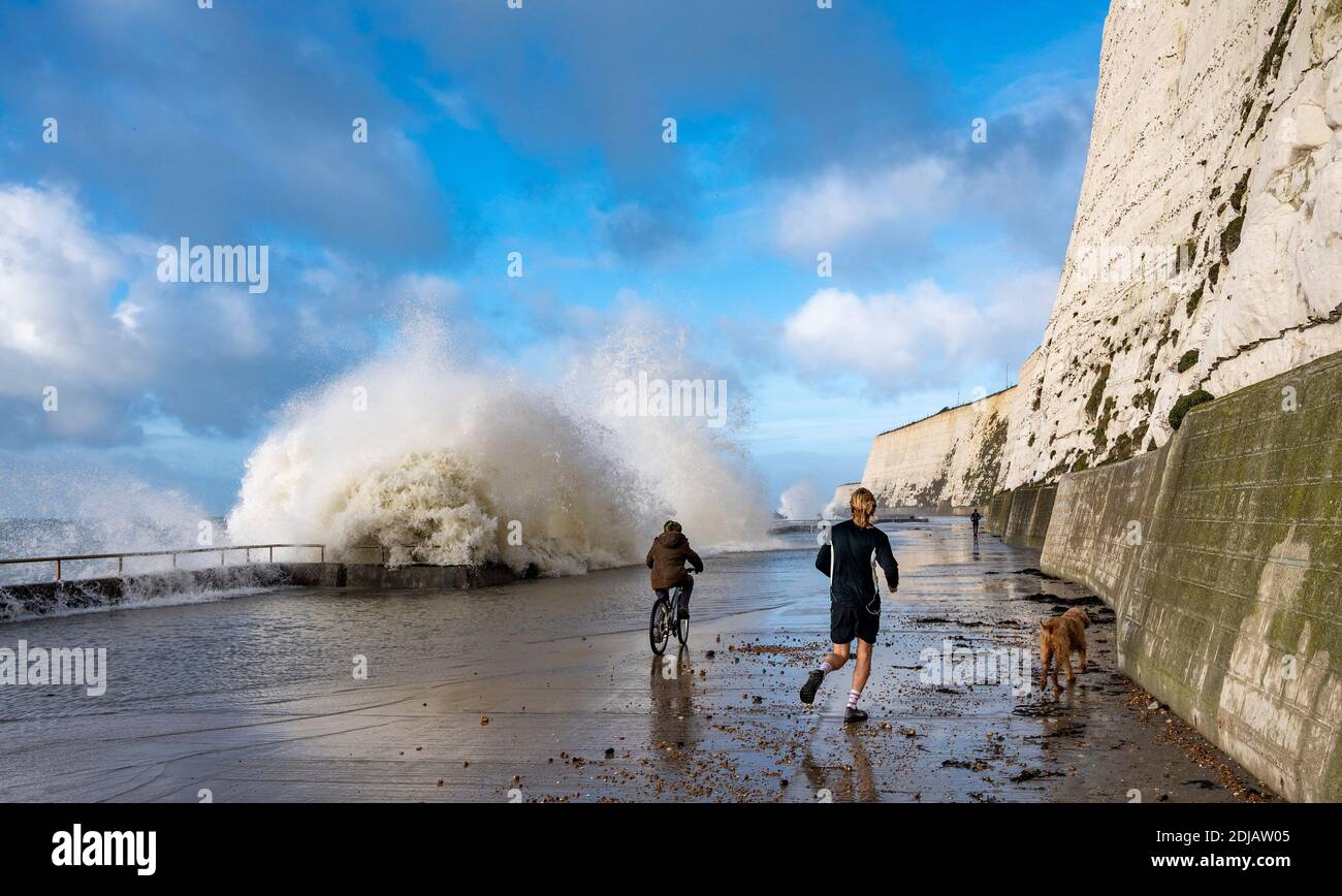 Brighton UK 14. Dezember 2020 - EIN Läufer und Radfahrer beobachten und ausweichen die Wellen in einem windigen Tag auf Saltdean undercliff Spaziergang an der Küste in der Nähe von Brighton bei Flut . Die Wettervorhersage ist für stärkere Winde und Duschen, um über Teile von Großbritannien zu verbreiten, aber mit Temperaturen, die wärmer als in den letzten Tagen sind : Credit Simon Dack / Alamy Live News Stockfoto